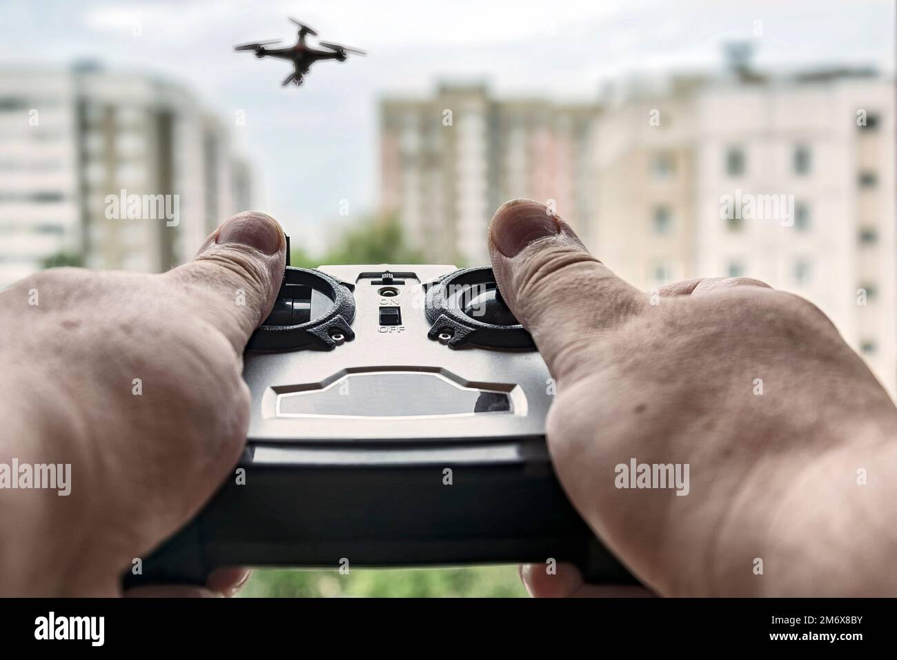 Hände halten die Drohne der Fernbedienung. Unscharfer Hintergrund mit Drohne und Häusern. Stockfoto