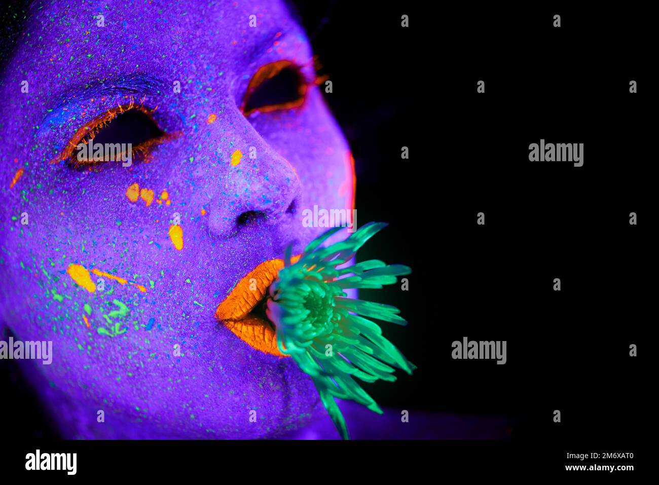 Seltsam und wundervoll. Eine junge Frau, die mit Neonfarbe im Gesicht posiert. Stockfoto