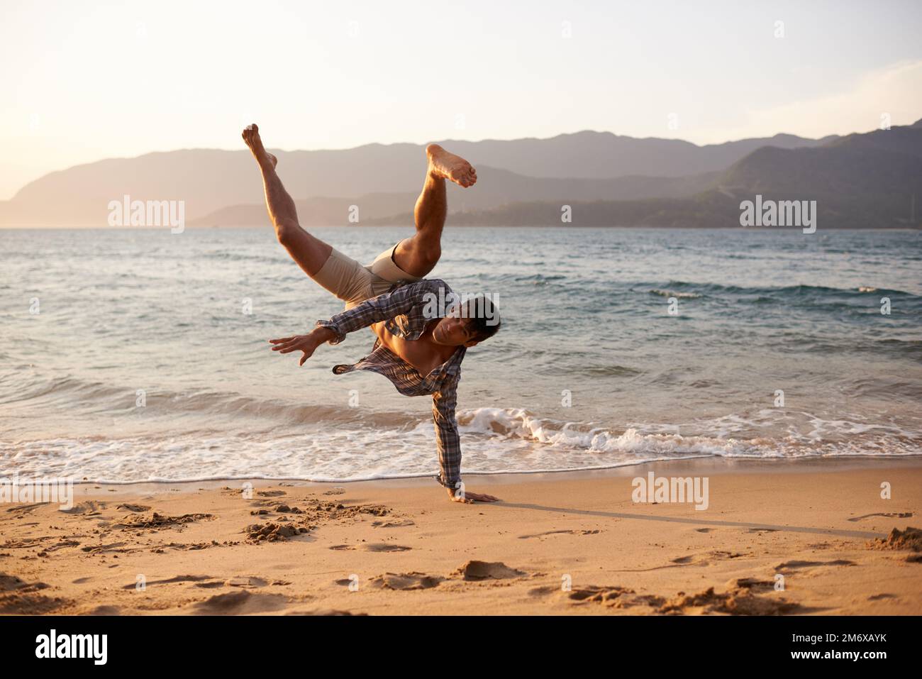 Seinen Breakdance zu veranstalten. Ein junger Mann, der am Strand tanzt. Stockfoto