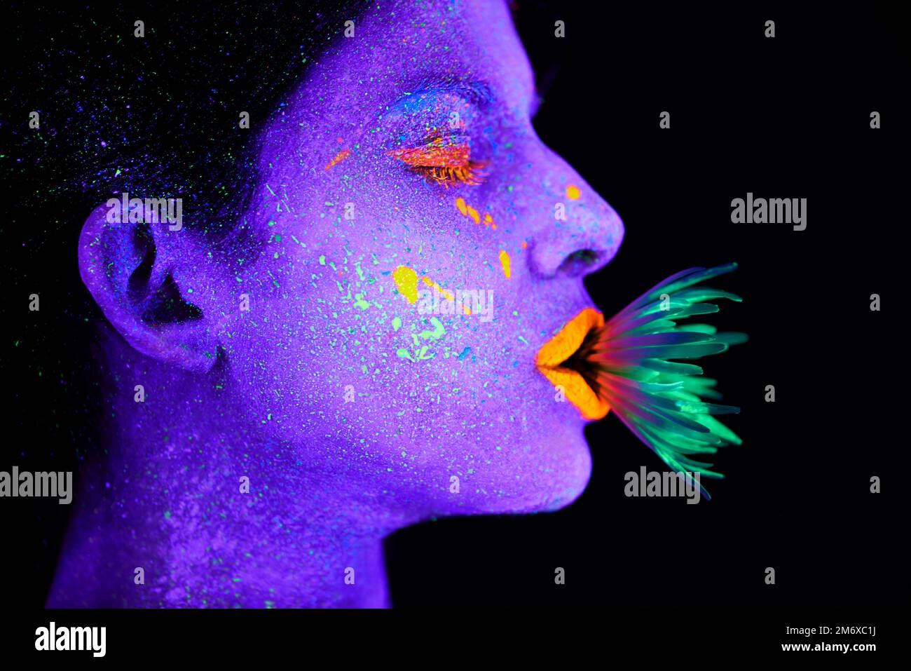 Unwirkliche Schönheit. Eine junge Frau, die mit Neonfarbe im Gesicht posiert. Stockfoto