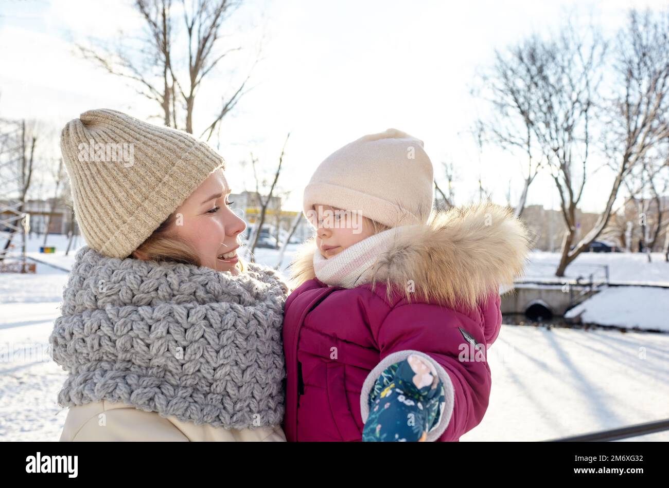Mutter und Tochter gehen an Weihnachten und Neujahr im winterlichen Stadtpark spazieren. Eltern und kleine Kinder haben Spaß im Freien Stockfoto