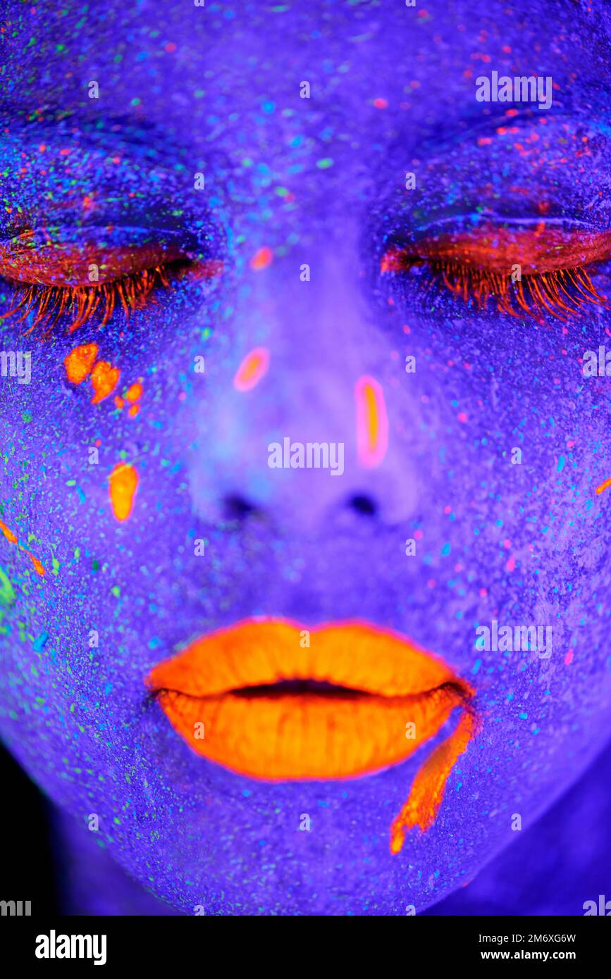 Glühende Göttin. Eine junge Frau, die mit Neonfarbe im Gesicht posiert. Stockfoto