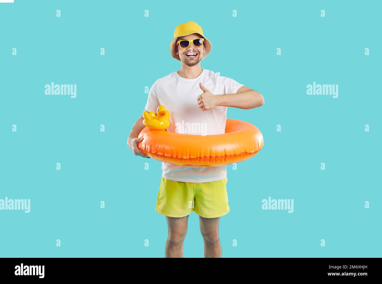 Ein fröhlicher Kerl mit lustigem aufblasbarem Kreis zum Schwimmen zeigt Daumen hoch auf hellblauem Hintergrund. Stockfoto