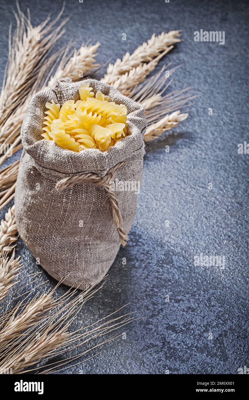 Hessischer Sack mit spiralförmigen Makkaroni-Weizen-Roggenohren auf schwarzem Hintergrund. Stockfoto