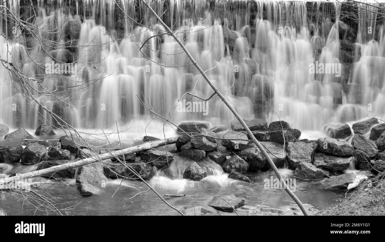 Wasserfall mit vielen Stufen hinter Ästen und Steinen in Österreich in Schwarz und Weiß Stockfoto