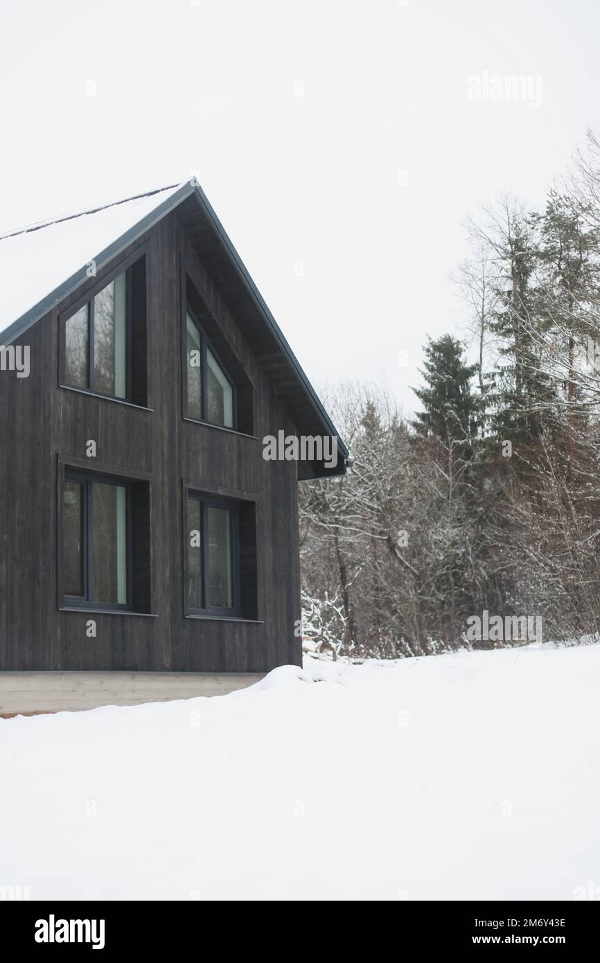 Das ist das Winterfest. Schwarze Hütte in einem wunderschönen Schneewald. Malerische Landschaft mit schwarzem Holzhaus im Winter. Stockfoto