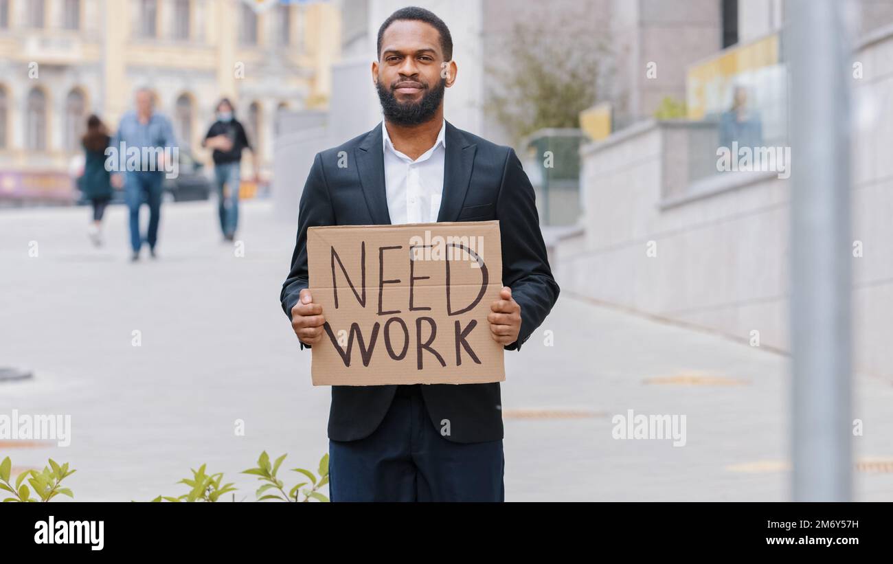 Ethnisch entlassener, bärtiger, gefeuerte, afroamerikanischer Mann männlicher Arbeiter in der Stadt, der Poster in der Hand hält, braucht Arbeit, um Kamera zu suchen, Jobangebot zu suchen Stockfoto