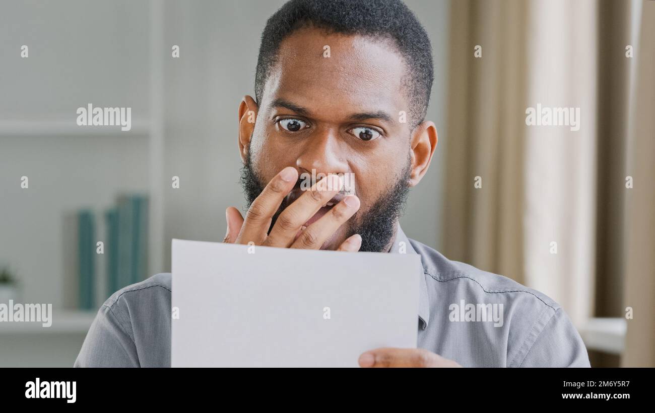 Unglücklicher Afroamerikaner schockierte gestresster bärtiger Mann im Büro, der schlechte Nachrichten liest, während er sich gestresst fühlt Stockfoto