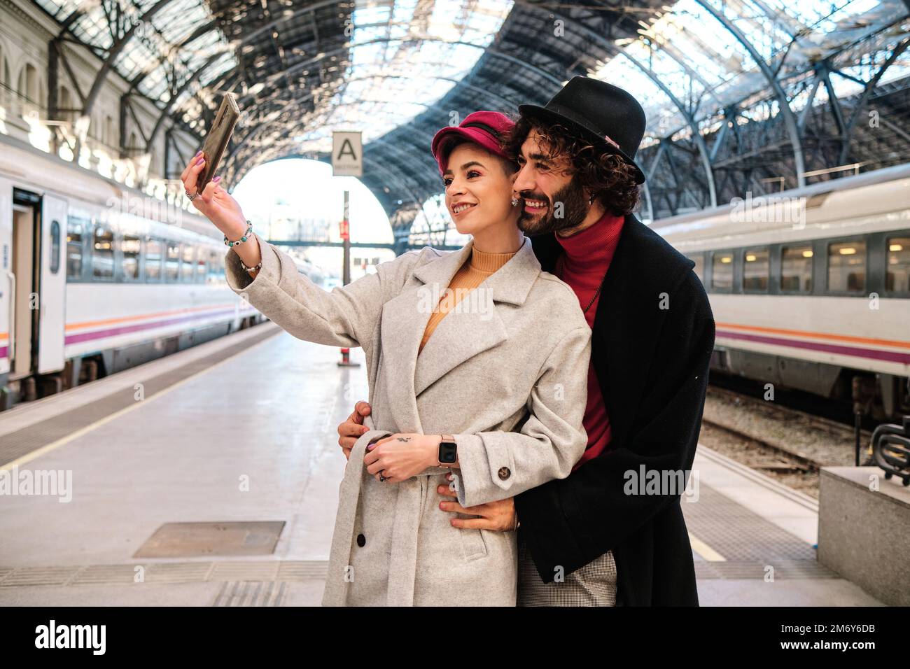 Ein Paar, das sich umarmt, während es ein Selfie in einem Bahnhof macht Stockfoto