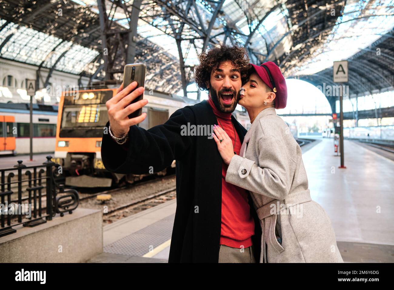 Ein Paar macht ein Selfie, während er sich in einem Bahnhof küsst Stockfoto