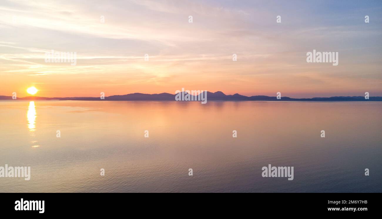 Blick auf die Papas von Jura, die Insel Jura und die Isle of Islay, Hebriden, Schottland von der Insel Gigha bei Sonnenuntergang Stockfoto