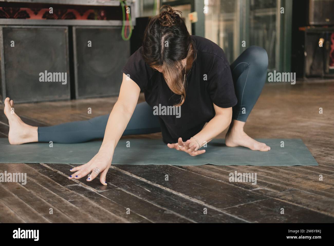 Frau Yoga und neue Lehrerin junger Erwachsener, die eine Skandasana-Pose machen und sich in eine andere Pose bewegen, tragen grüne Leggings während ihres Yoga-Trainings auf einer Woode-Matte Stockfoto