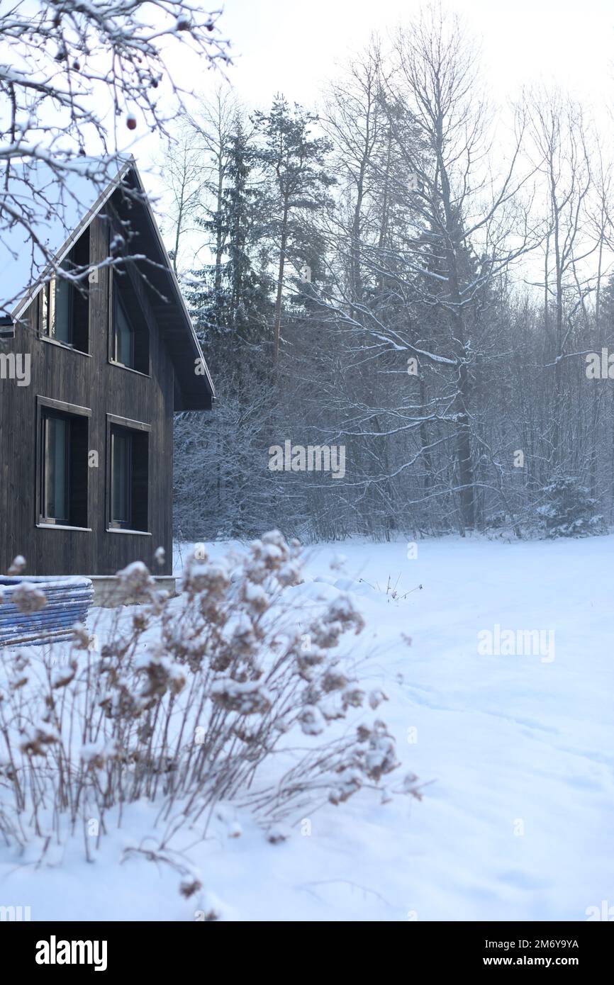 Das ist das Winterfest. Schwarze Hütte in einem wunderschönen Schneewald. Malerische Landschaft mit schwarzem Holzhaus im Winter. Stockfoto