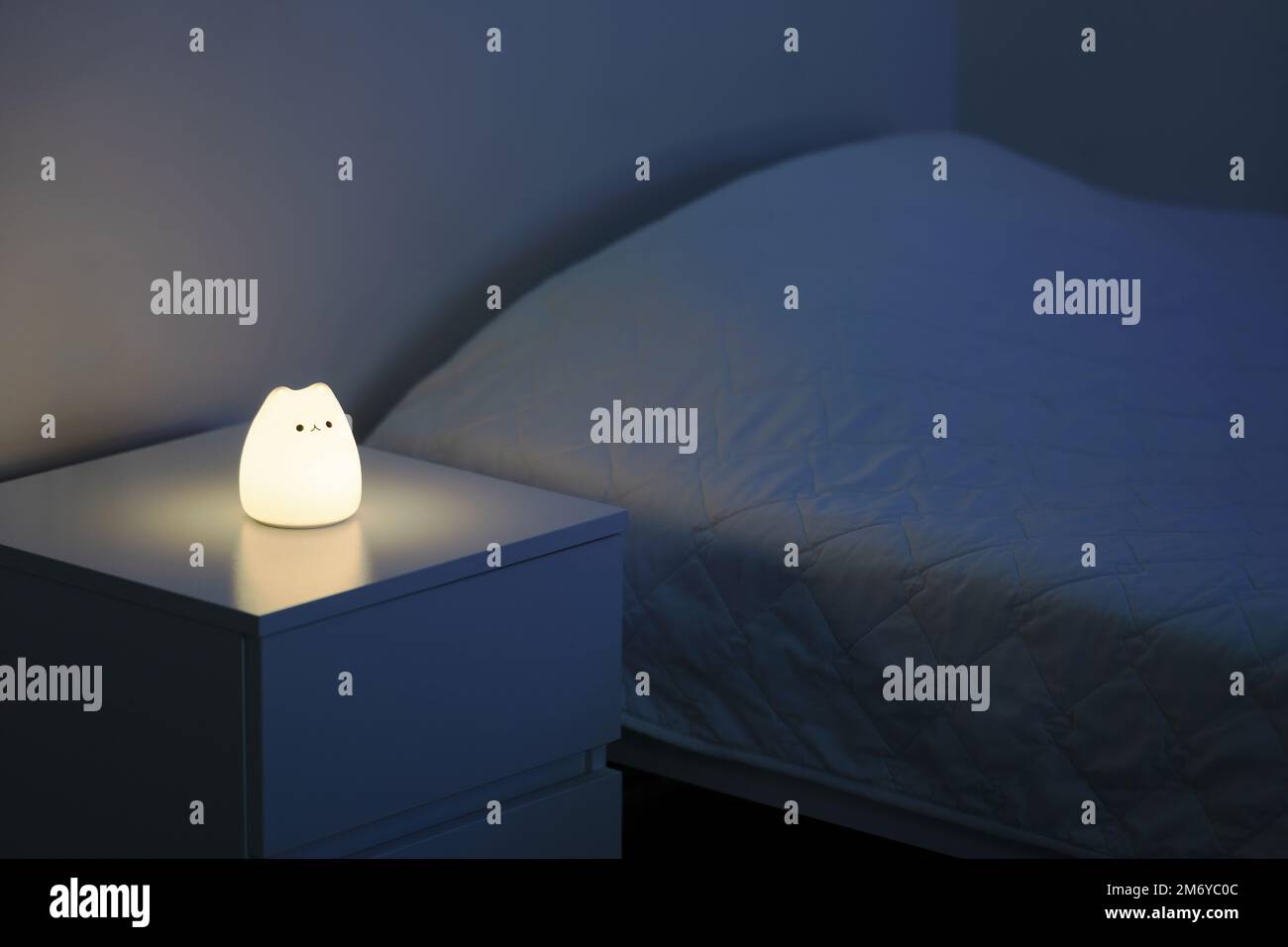 Süße katzenförmige Nachtlampe, die auf einem Nachttisch neben dem Bett steht. Nachttischlampe. Nachtlampe steht neben dem Bett. Die Schlafzimmerlampe liegt auf einem Nachttisch Stockfoto