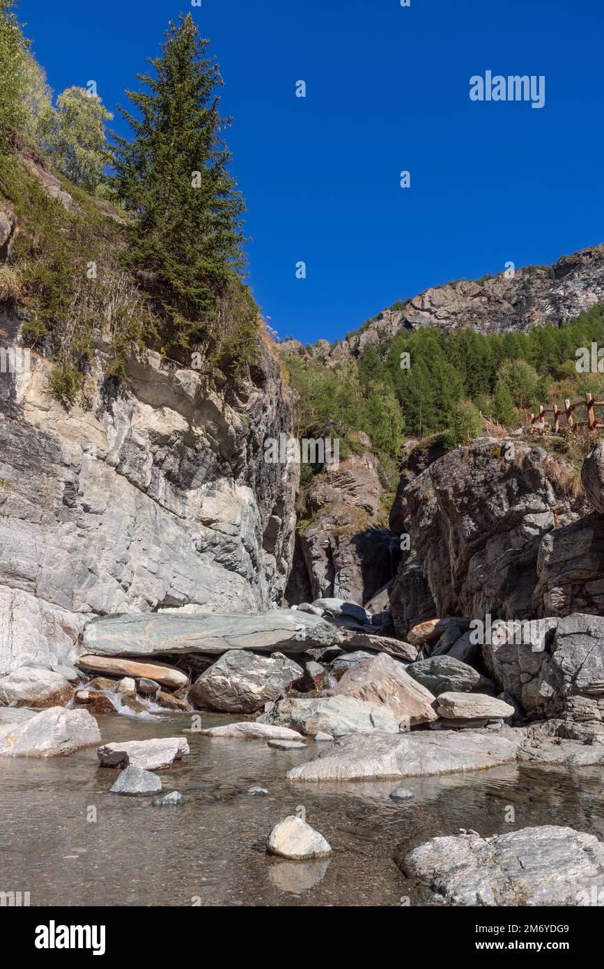 Wunderschöne Aussicht auf den Teich mit kristallklarem fließendem Wasser, geformt vom Lillaz-Wasserfall (Cascate di Lillaz), Wanderweg mit Holzgeländer entlang der Risse Stockfoto