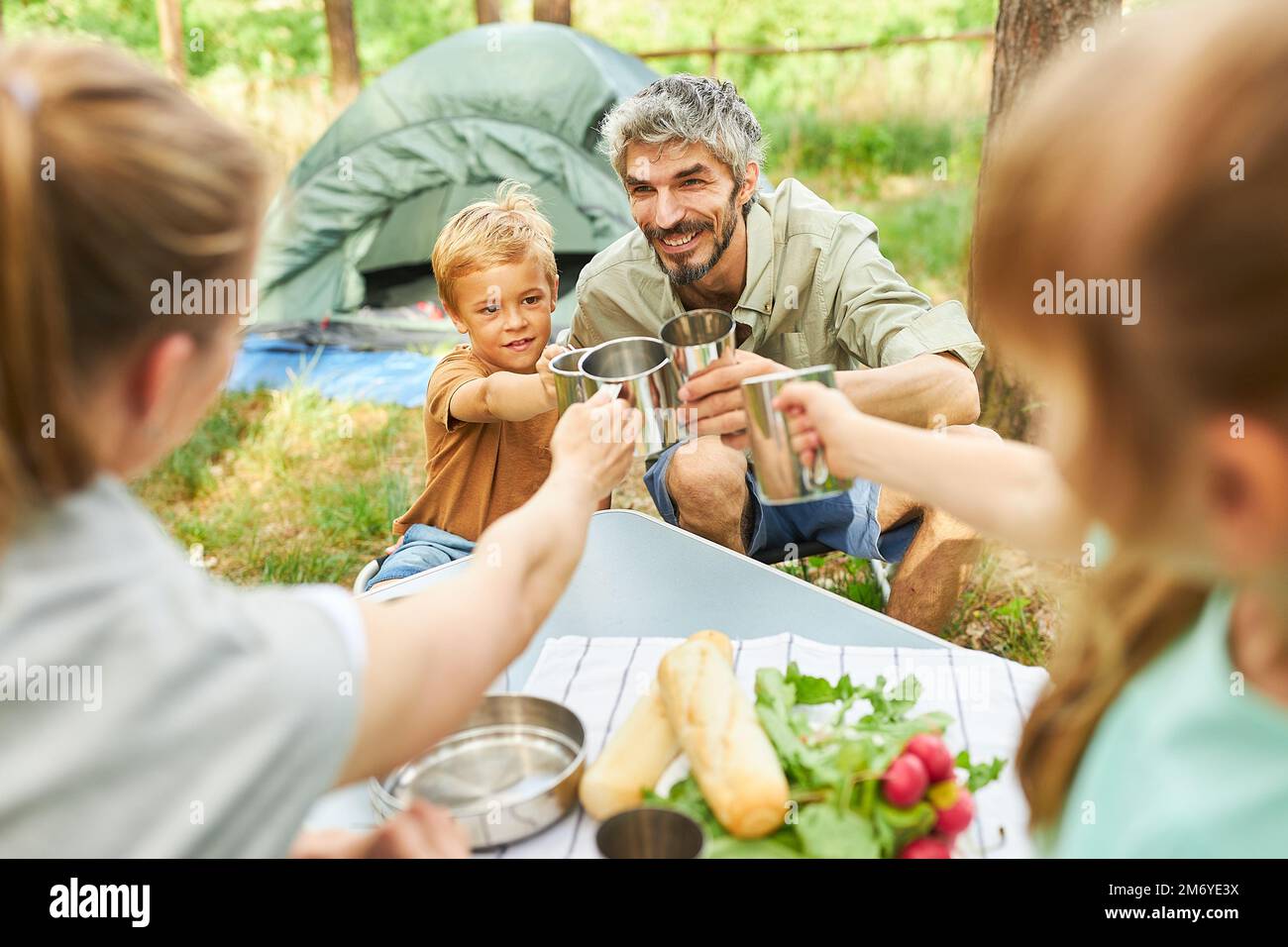 Glückliche Eltern toasten mit Kindern Tassen, während sie im Urlaub im Wald campen Stockfoto