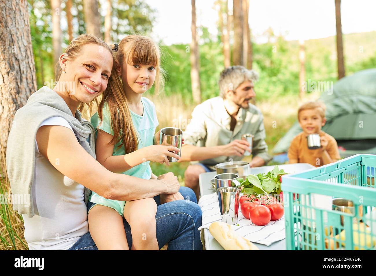 Porträt von Mutter und Tochter mit Familie im Hintergrund, die beim Picknick frühstücken Stockfoto