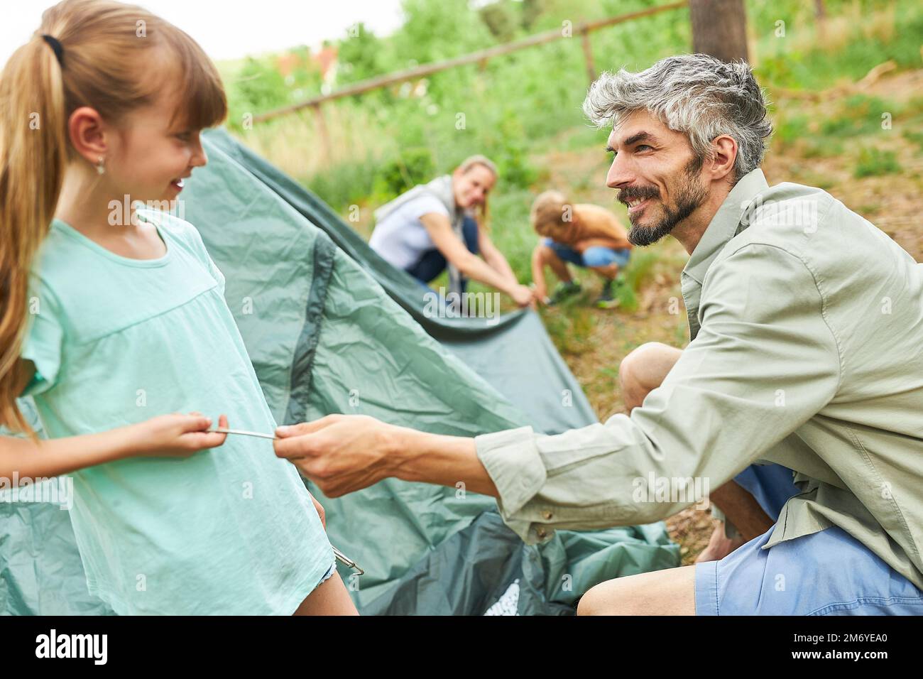 Lächelnde Tochter hilft Vater beim Aufbau eines Zeltes während der Sommerferien im Wald Stockfoto