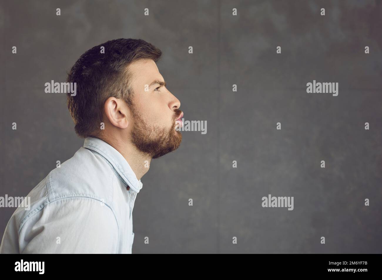 Profilporträt eines Mannes, der Lippen schmollt, einen Kuss gibt oder einen Luftkuss auf der leeren Seite bläst Stockfoto