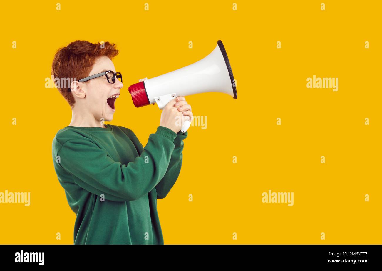 Glückliches Schulkind in Brille schreit durch Megafon auf gelbem Studiohintergrund Stockfoto