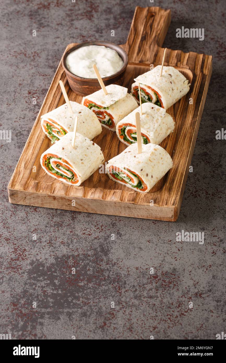 Norwegische Rolle mit geräuchertem Lachs, Frischkäse und Kräutern, in flaches Brot eingewickelt, Nahaufnahme auf einem Holzbrett auf dem Tisch. Vertikal Stockfoto