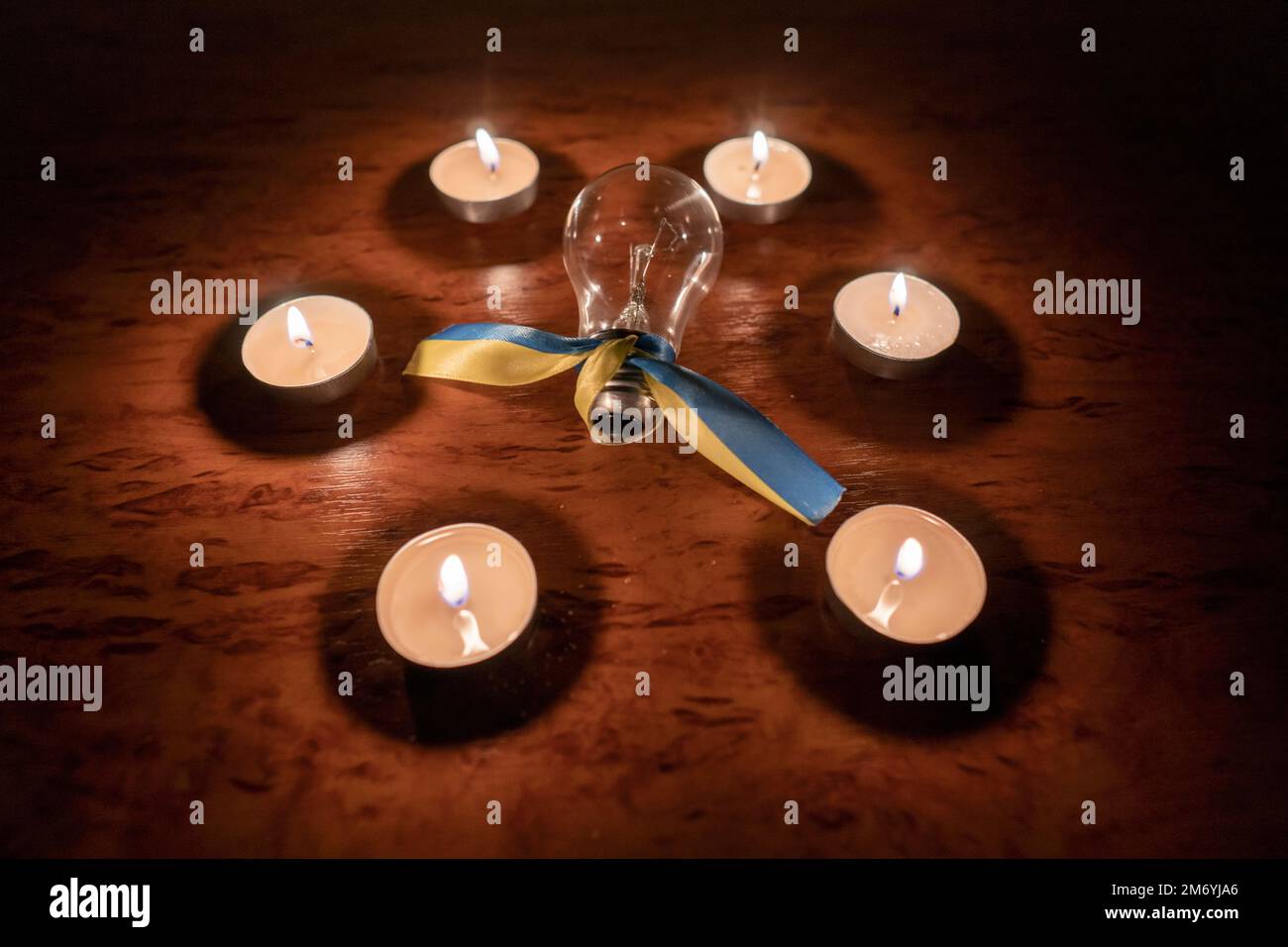 Elektrische Glühbirne mit einem gelb-blauen Band (nationales Symbol der Ukraine) in einem Kerzenkreis. Stromausfall. Energiekrise. Stromausfallkonzept Stockfoto