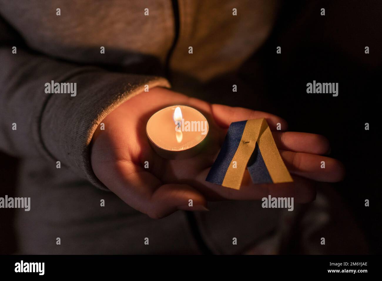 Das Mädchen hält eine brennende Kerze und ein gelb-blaues Band in den Händen (nationales Symbol der Ukraine). Stromausfall. Energiekrise. Stromausfallkonzept Stockfoto