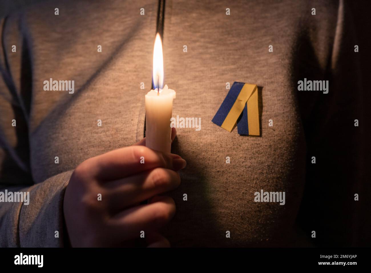 Ein Mädchen mit einem gelb-blauen Band (nationales Symbol der Ukraine) hält eine brennende Kerze in der Hand. Stromausfall. Energiekrise. Stromausfallkonzept Stockfoto
