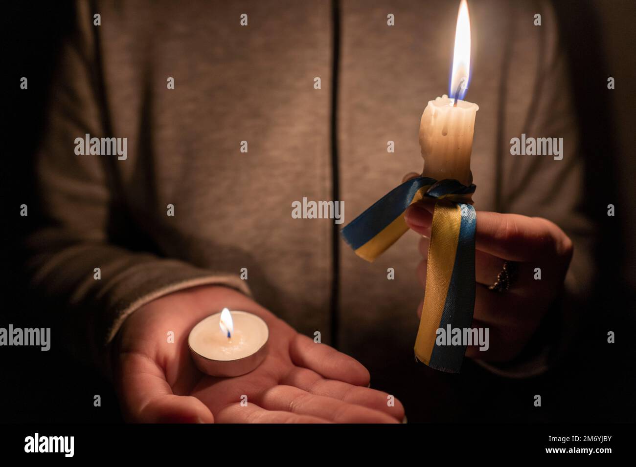 Stromausfall. Energiekrise. Stromausfallkonzept. Mädchen hält zwei brennende Kerzen mit einem gelb-blauen Band in der Hand (das nationale Symbol der Ukraine) Stockfoto