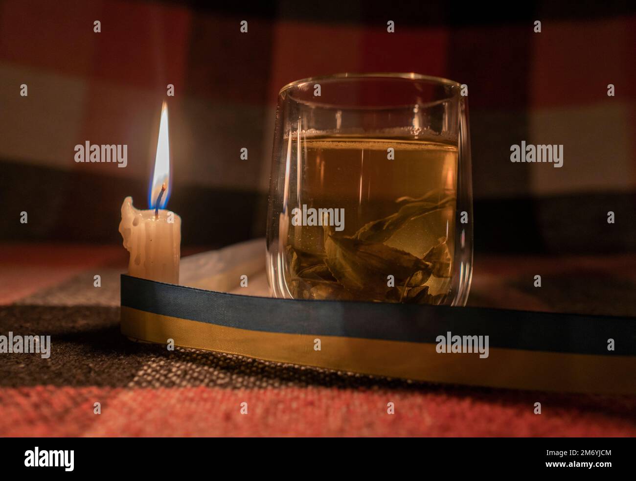Stromausfall. Stromausfallkonzept. Transparente Tasse Kräutertee im Licht einer brennenden Kerze mit einem gelb-blauen Band (nationales Symbol der Ukraine) Stockfoto