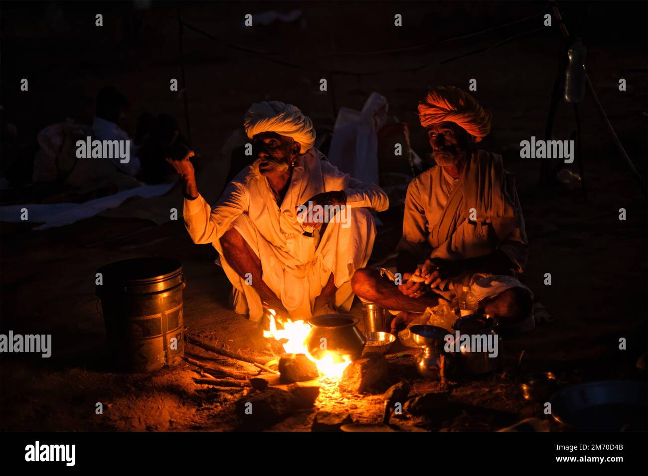 Pushkar, Indien - 6. November 2019: Indische Landdorfbewohner und Kamele, die nachts auf der Kamelmesse Pushkar Mela vom Lagerfeuer angezündet werden - jährlich berühmtes Ca Stockfoto