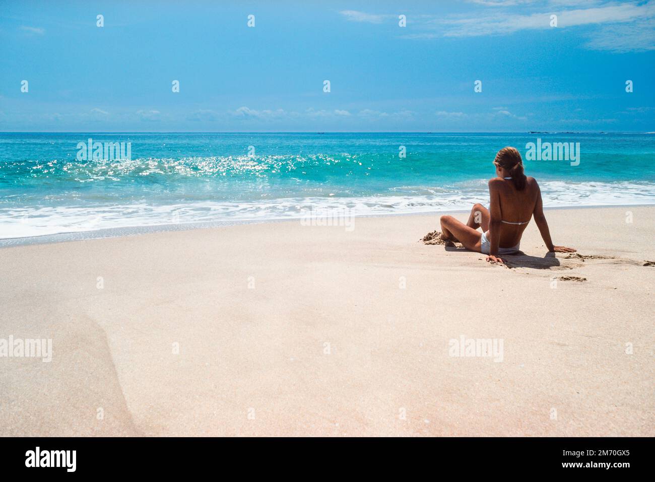 Tropischer Strandurlaub, Rückansicht einer jungen Frau, die allein an einem einsamen weißen Sandstrand sitzt und auf den Indischen Ozean, Tangalle, Sri Lanka blickt Stockfoto