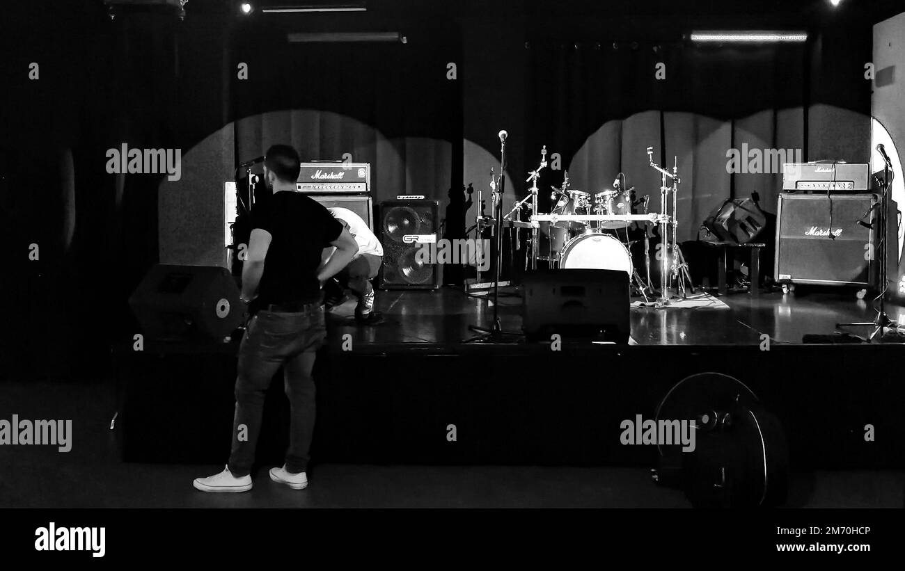 Eine Graustufenaufnahme, die die Bühne für eine Live-Show einer Rockband in einem Saal bereitet Stockfoto
