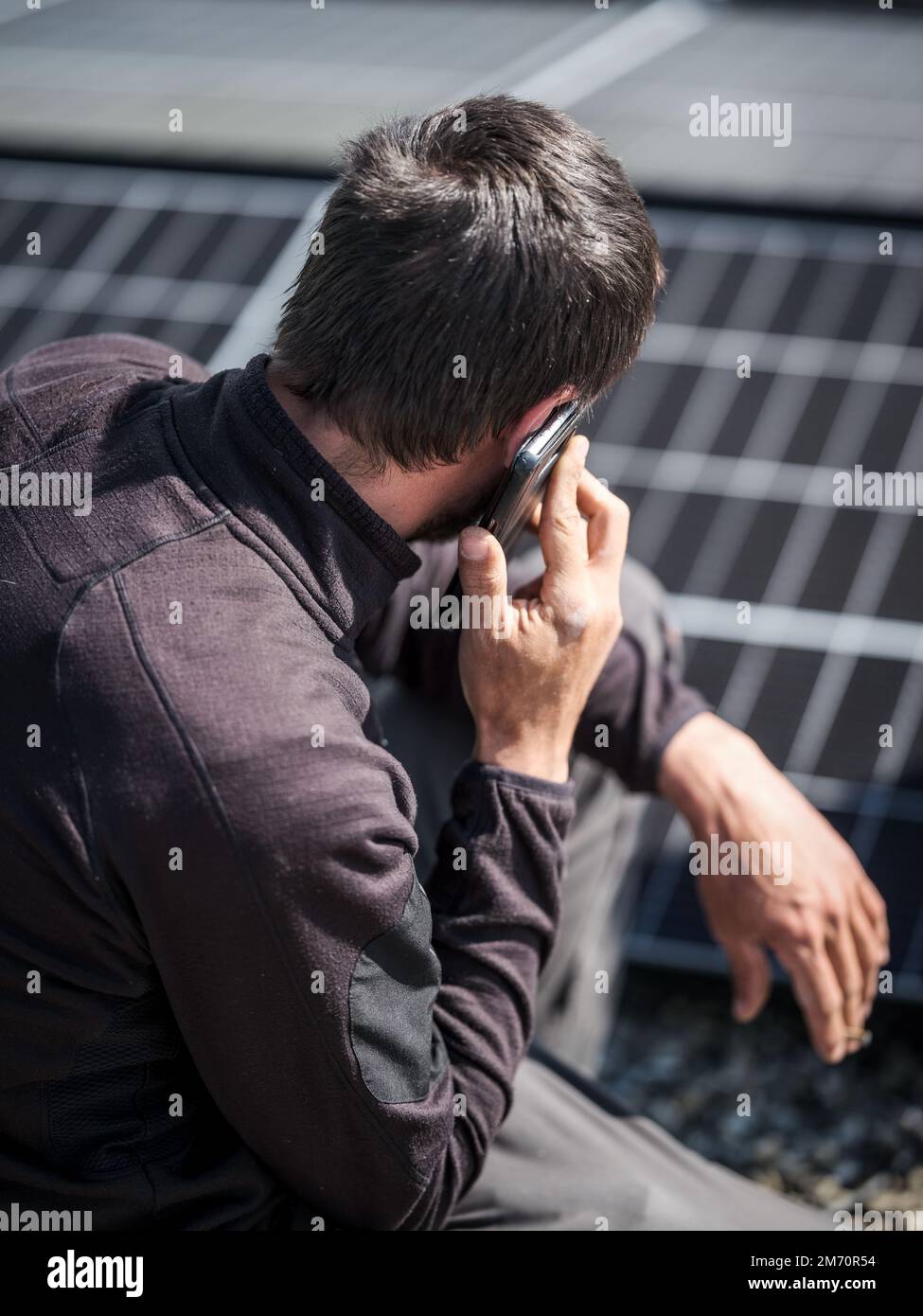 Dacharbeiter, der während der Installation von Solarpaneelen mit dem Mobiltelefon telefoniert Stockfoto