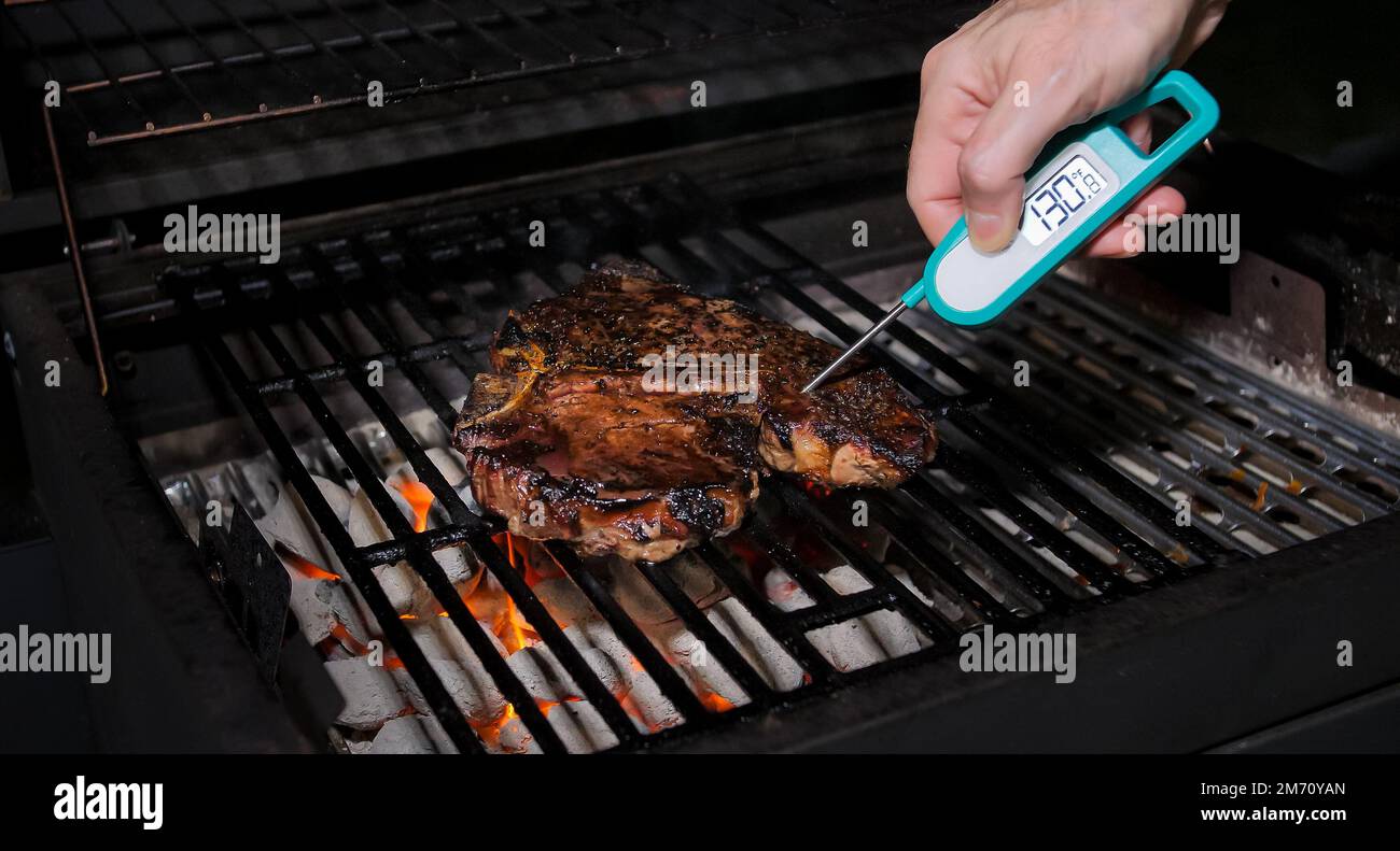 Prüfen der sicheren Lebensmitteltemperatur mit einem digitalen Sofortthermometer. Kochen Sie die Temperatur des frisch gegrillten Steaks auf dem heißen Grill. Stockfoto