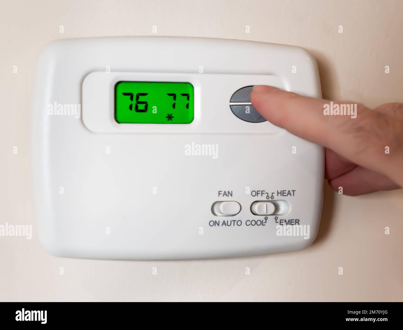 Nahaufnahme der Hand eines Mannes, der die Raumtemperatur mit einem programmierbaren Hausthermostat einstellt. Stockfoto