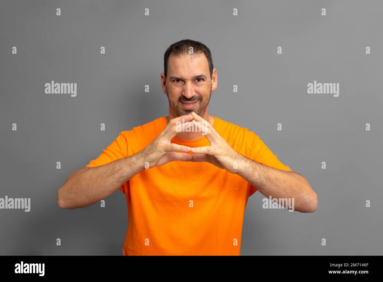 Böses Genie, intriganter Mann, Pläne schmieden, schlau und aufmerksam aussehen, eine Superhirn-Idee, beim Denken mit den Fingern kippen, gegen Grau stehen Stockfoto