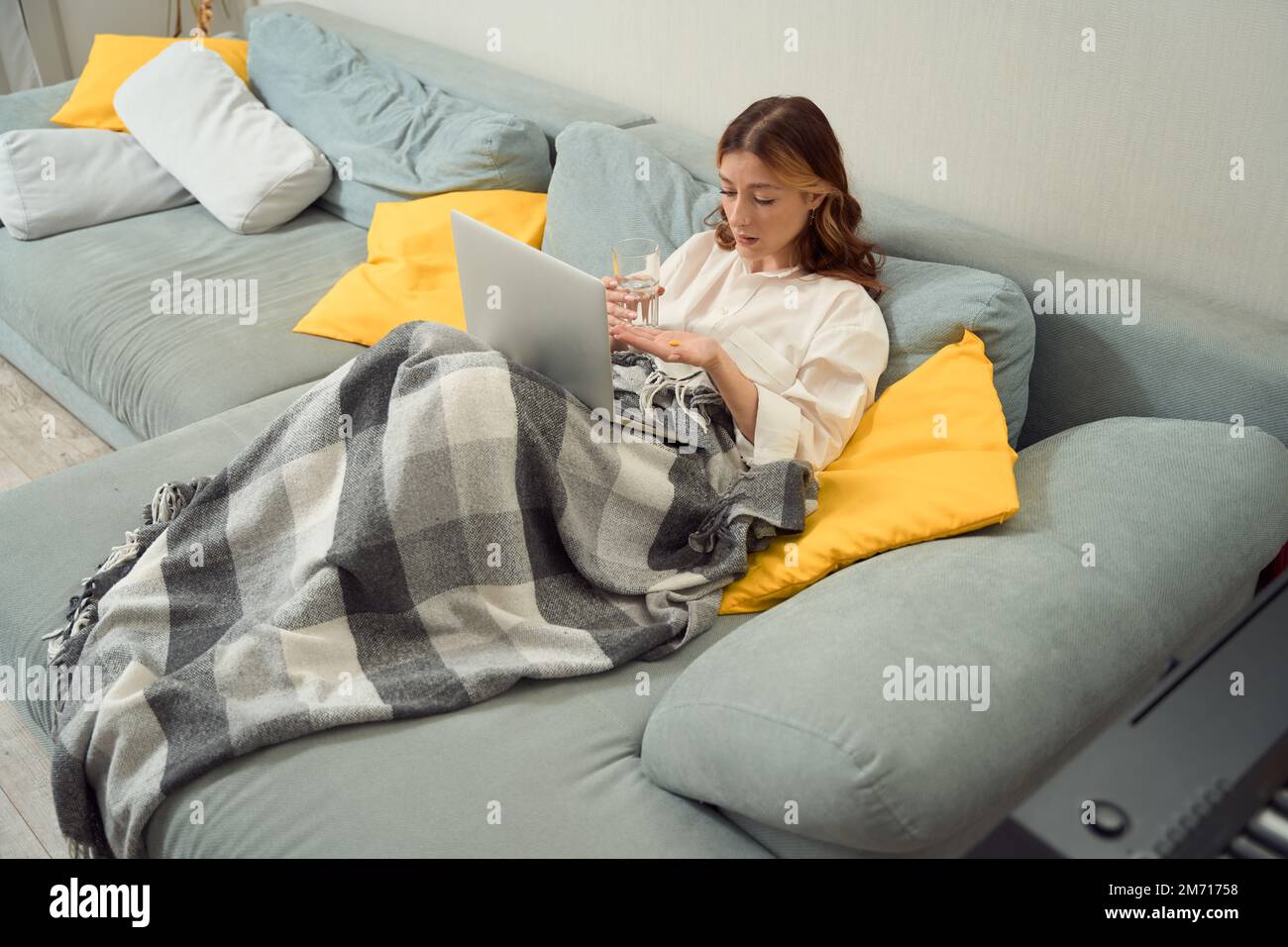 Kranke junge Frau, eingewickelt in Karo, die sich auf die Einnahme von Medikamenten vorbereitet Stockfoto