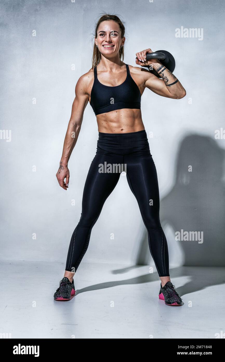 Sportliche Frau, die sich nach dem Training mit Kugelhantel ausruht. Foto einer Frau mit perfekter Figur auf grauem Hintergrund. Stärke und Motivation Stockfoto