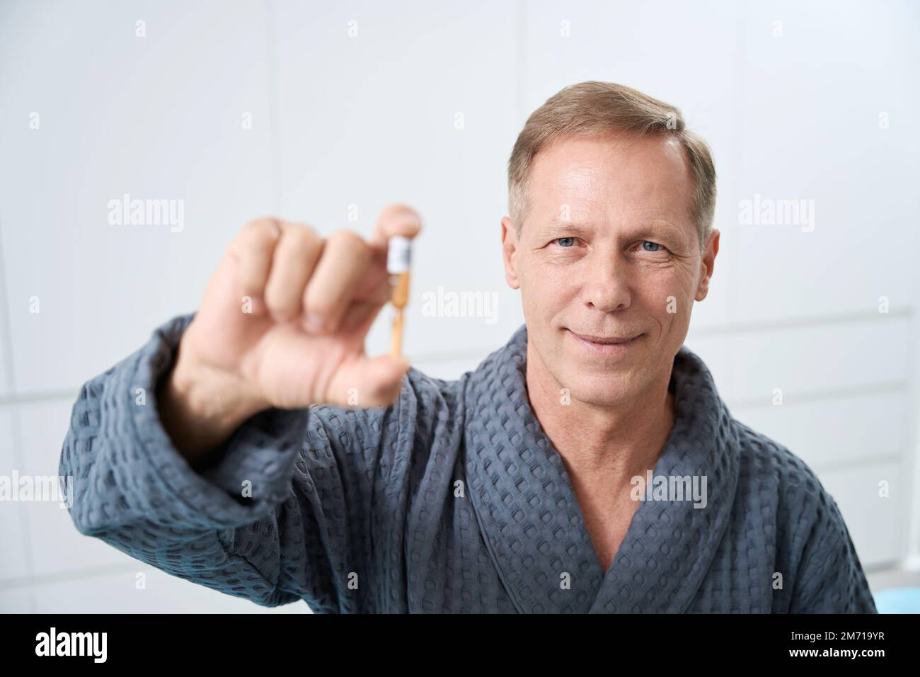 Ein angenehmer Mann mittleren Alters hält eine Ampulle Medizin in seinen Händen Stockfoto