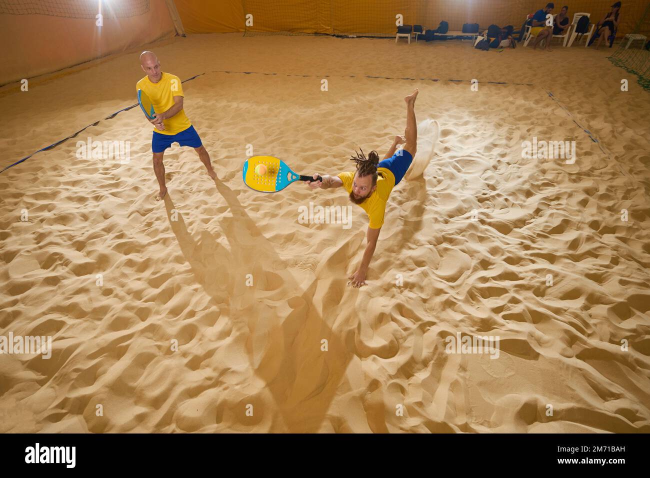 Zwei Spielkameraden fangen einen Tennisball im Sand Stockfoto