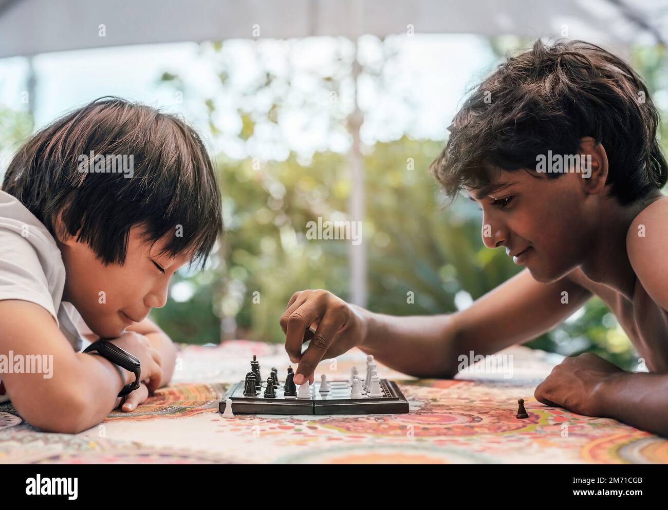 Zwei Jungs spielen Schach im Garten. Die Jungs sind indischer und chinesischer Herkunft. Der Begriff der kulturellen Vielfalt und der ethnischen Zugehörigkeit Stockfoto