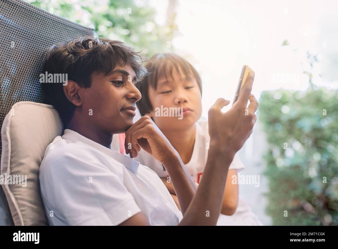 Zwei Jungs unterschiedlicher Herkunft sehen sich das Handy merkwürdig an. Die Jungs sind chinesischer und indischer Herkunft. Kulturelle Vielfalt und multiethnisches Konzept. Stockfoto