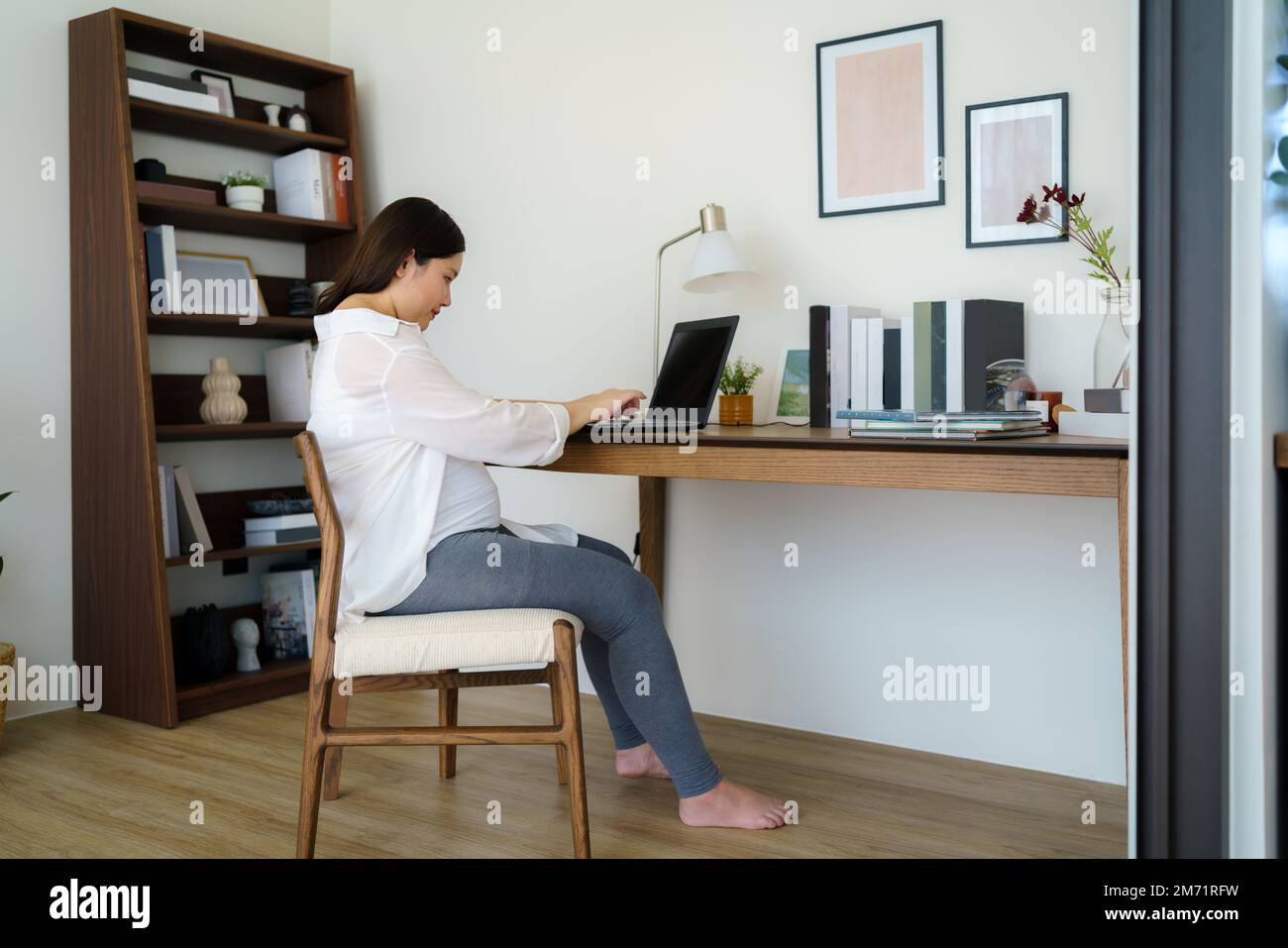 Asiatische Schwangere, die während des Mutterschaftsurlaubs einen Laptop an ihrem Wohnzimmertisch zu Hause benutzt. Stockfoto