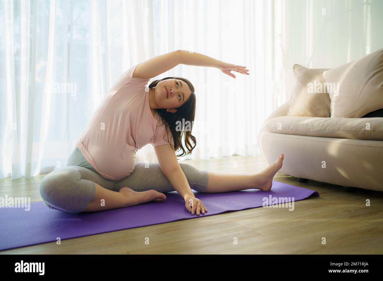 Porträt einer asiatischen Schwangeren, die Yoga im Wohnzimmer praktiziert. Stockfoto