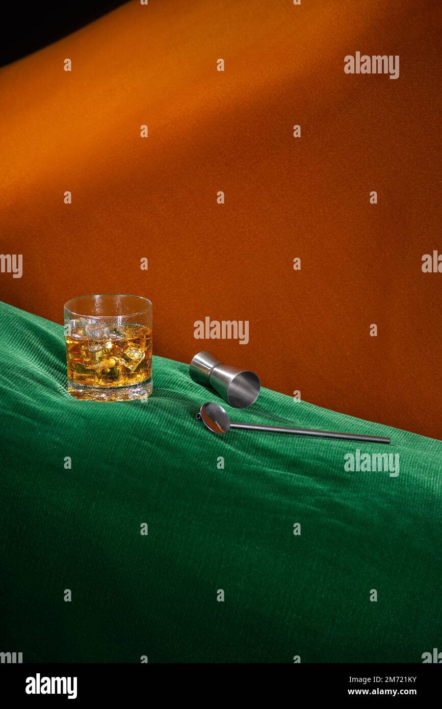 Alkoholisches Getränk mit Eis auf einem grün-orangefarbenen abstrakten Raum mit Barkeeper-Kit, keine Menschen Stockfoto