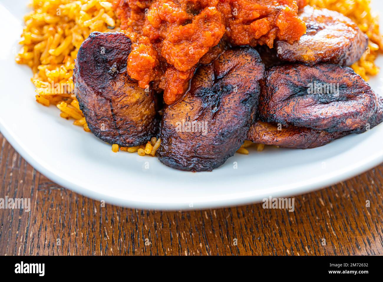 nigerianischer Jollof Reis serviert mit Plantain und Eintopf Stockfoto