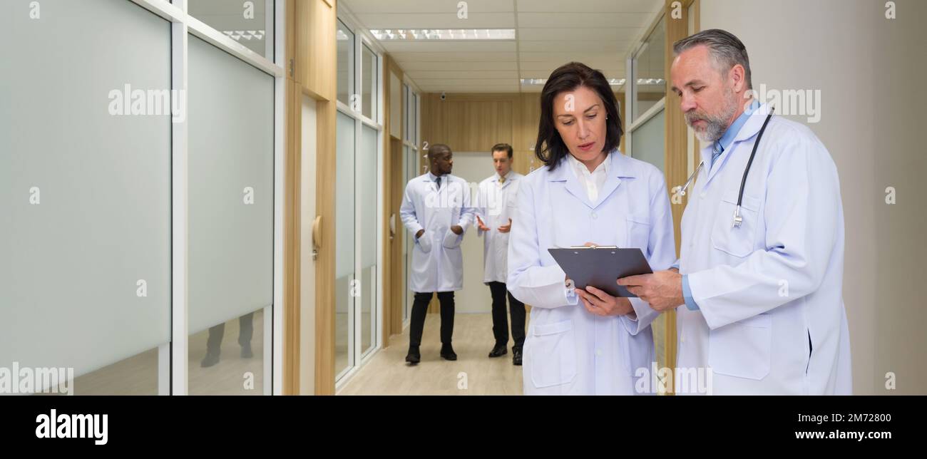 Senior Professorin konsultiert eine Ärztin vor dem Zimmer eines Krankenhauspatienten. Beide achten auf das Dokument in der Zwischenablage. Zwei Doc Stockfoto