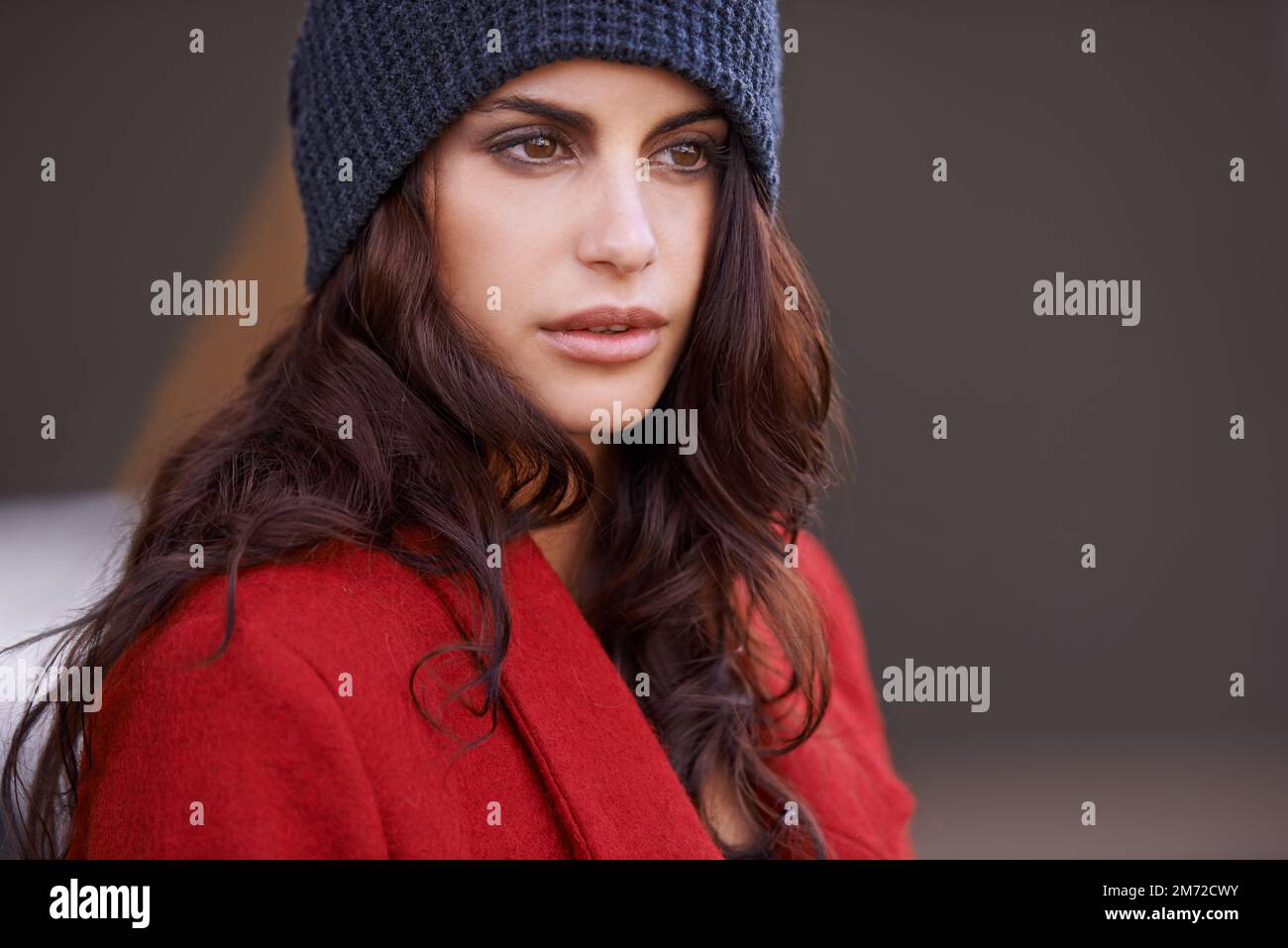 Scharlachrote Stunner. Eine schöne junge Frau, die einen roten Wintermantel und eine Mütze trägt. Stockfoto