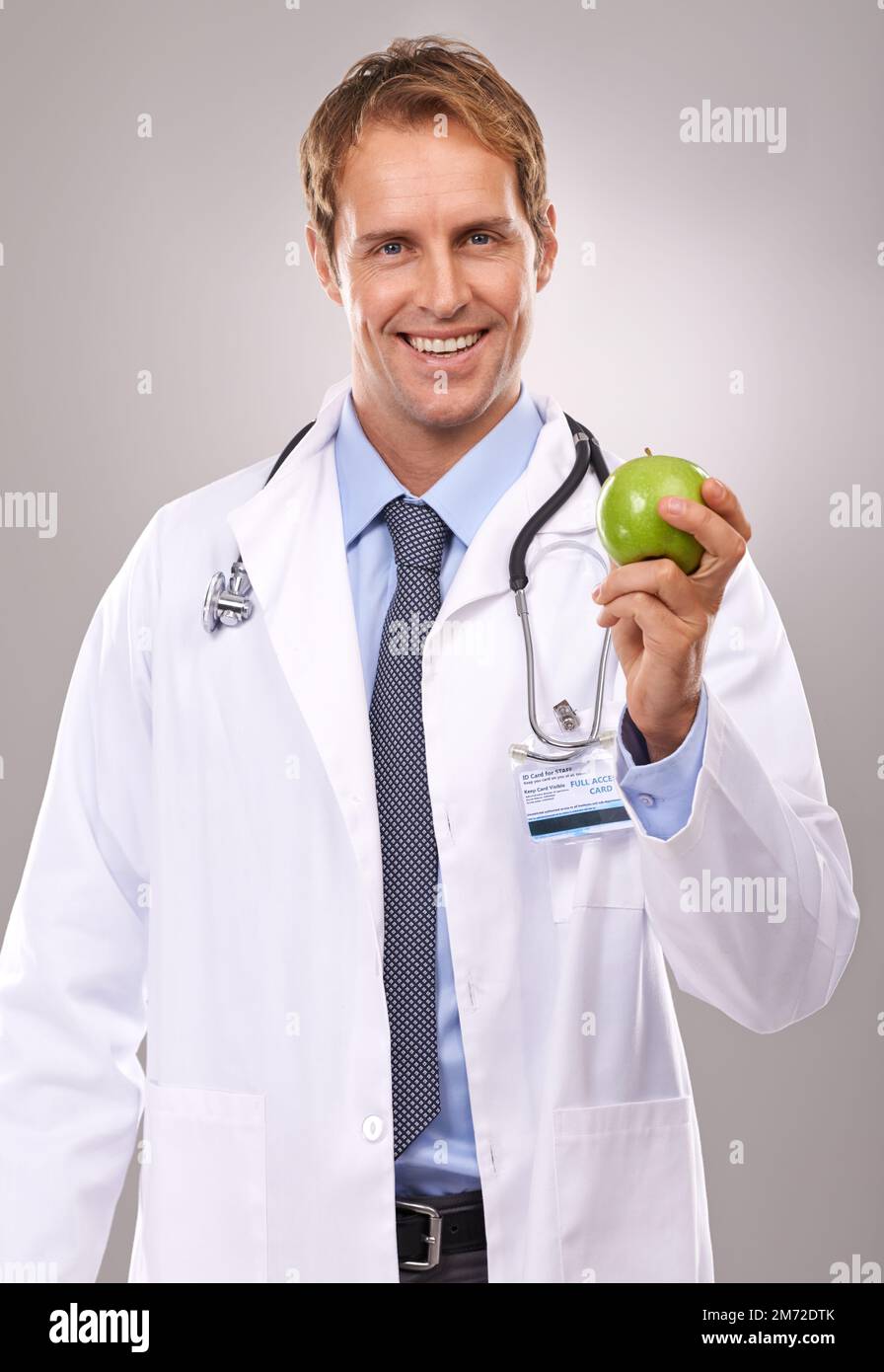 Eine pro Tag... Ärztliche Anweisung. Porträt eines gutaussehenden jungen Arztes, der einen grünen Apfel hält. Stockfoto